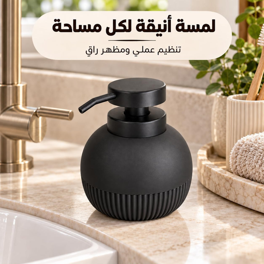 A matte black spherical soap dispenser with a ribbed base and curved pump, placed on a marble bathroom counter beside a brass faucet. Arabic text appears at the top, and a small plant and towel are visible in the background.