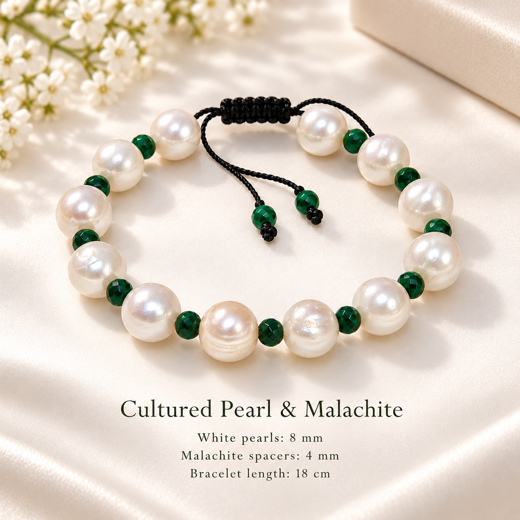 A pearl and malachite beaded bracelet displayed on a cream satin surface with small white flowers in the corner. The bracelet features large white pearls and dark green malachite beads separated by black cord.