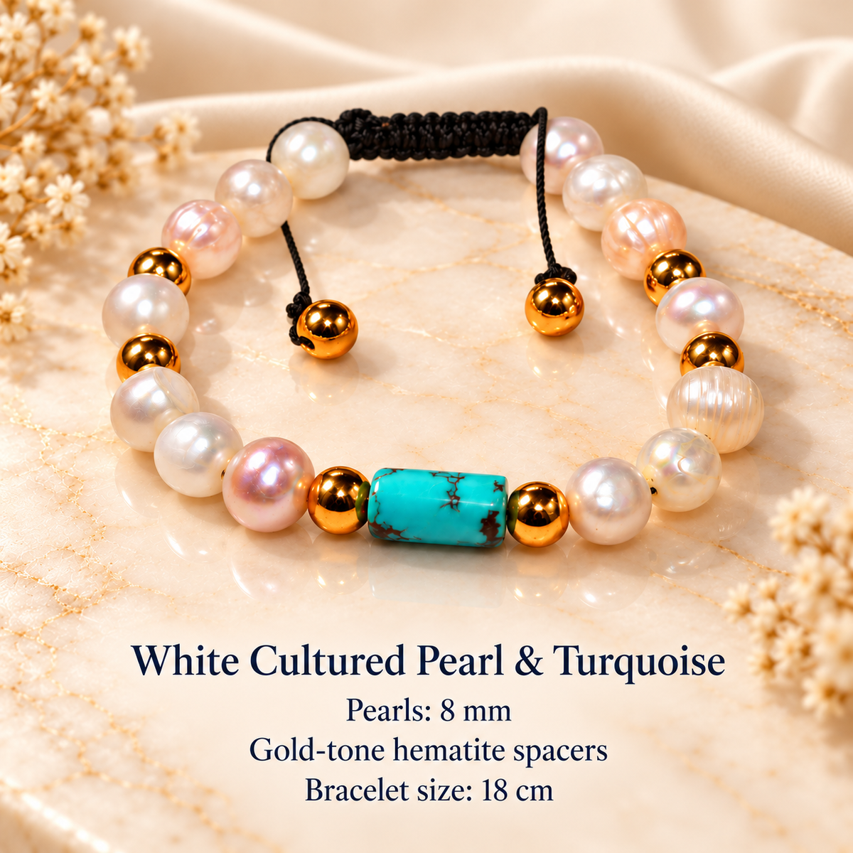 A beaded bracelet displayed on a beige marble slab with dried flowers. The bracelet features white cultured pearls, a turquoise-colored heart-shaped bead, gold-tone spacer beads, and a black adjustable cord.