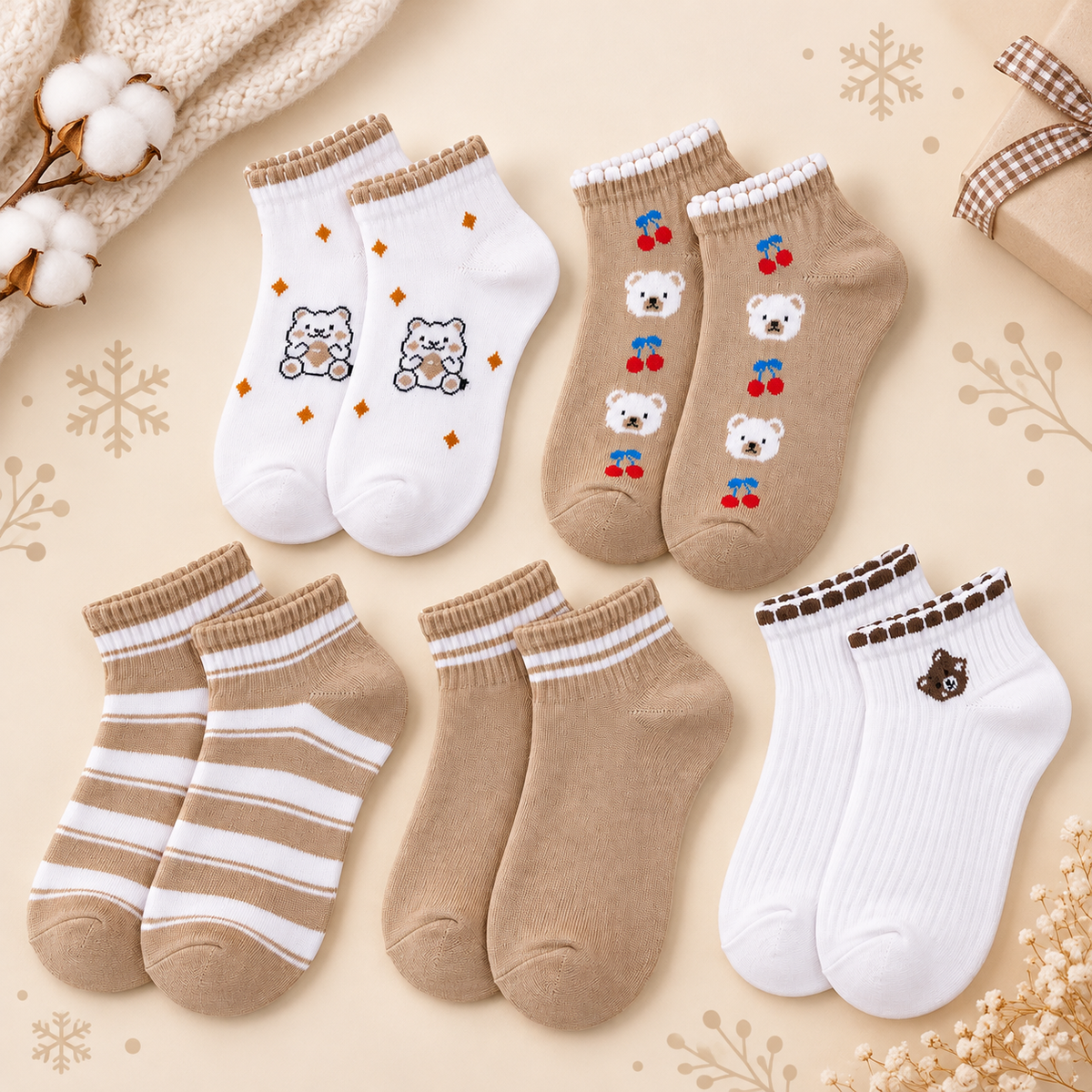 Six pairs of children's ankle socks arranged on a beige background with decorative winter-themed props. The socks include white pairs with tan stripes, tan pairs with white stripes, tan pairs with bear and cherry prints, and white pairs with a bear face print.