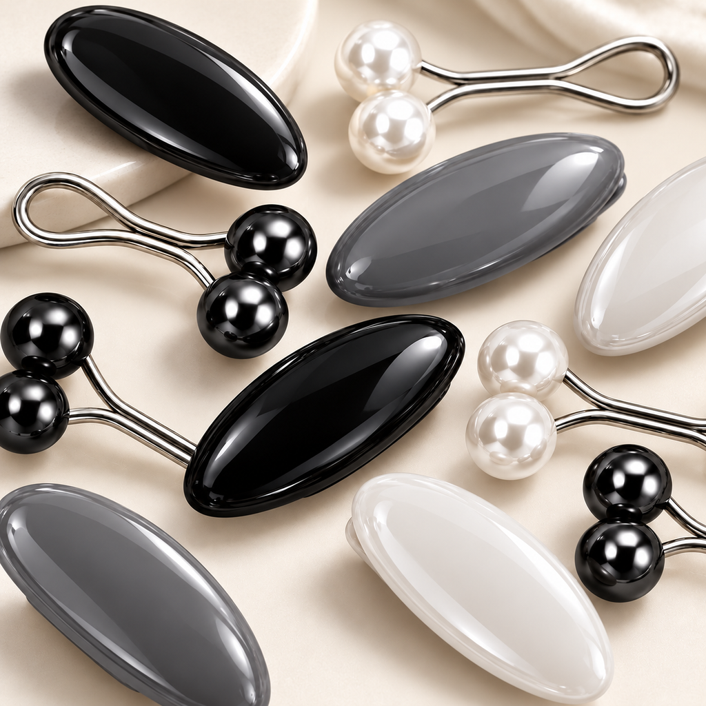 A set of massage tools featuring smooth oval heads in glossy black, matte gray, and pearlescent white, with some pieces showing dual pearl-like spheres connected by silver metal arms, arranged on a light beige fabric background.