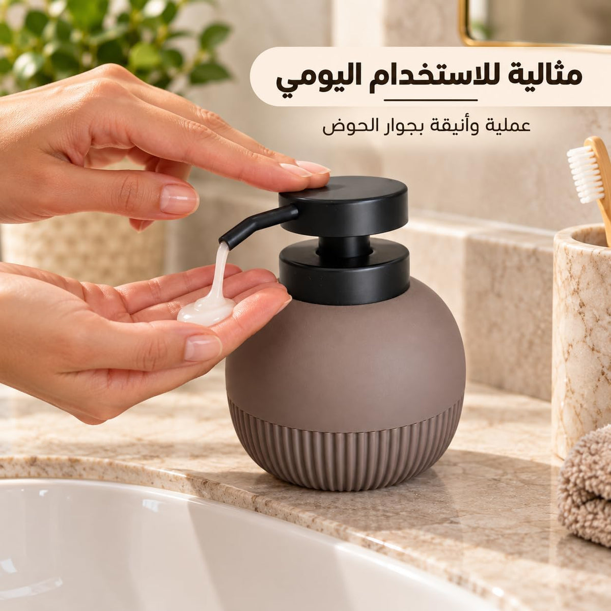 A matte taupe round soap dispenser with a black pump being used to dispense lotion into a hand, set on a bathroom counter next to a sink and toothbrush holder.