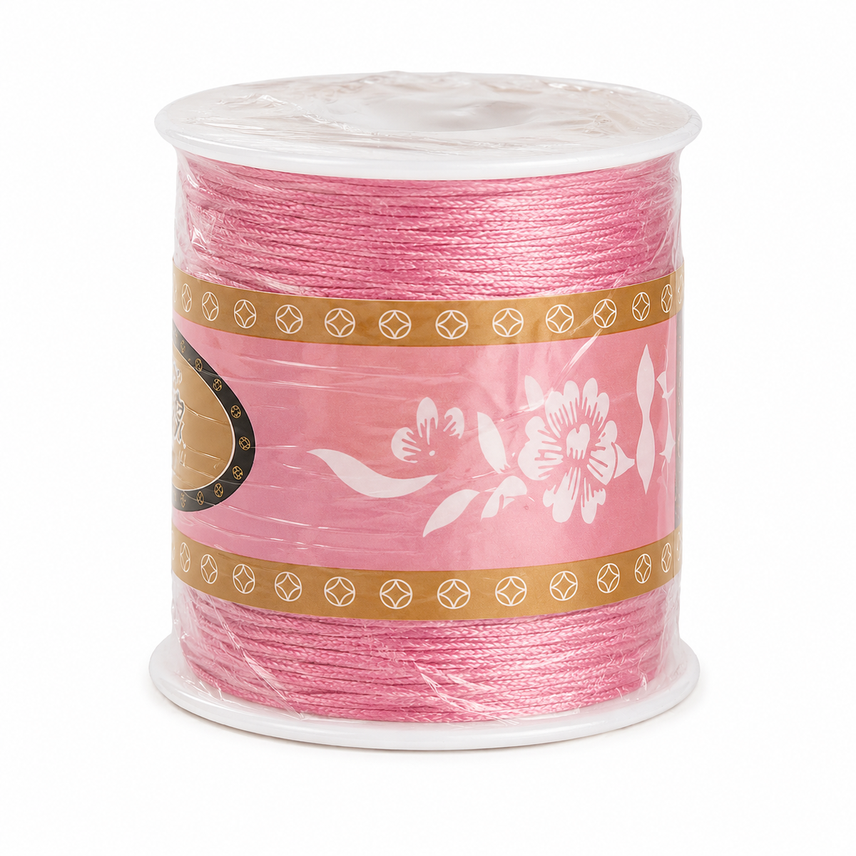 A spool of pink cord or thread wrapped in clear plastic with a decorative pink paper label featuring white floral motifs and gold geometric borders, shown on a plain white background.