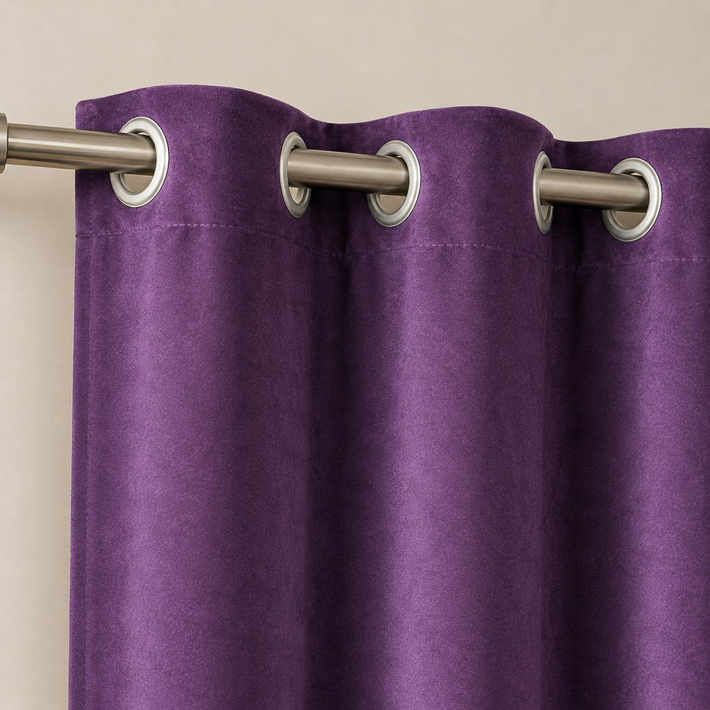 A close-up of a purple grommet curtain hanging from a silver metal rod against a plain beige wall.