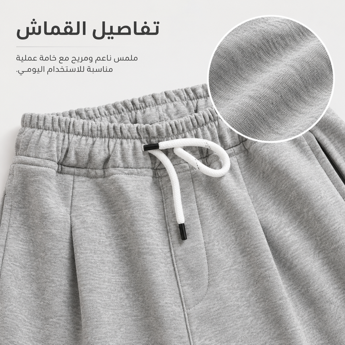 Close-up of light gray sweatpants with a white drawstring and a circular fabric texture inset, with Arabic text describing the material and fit.