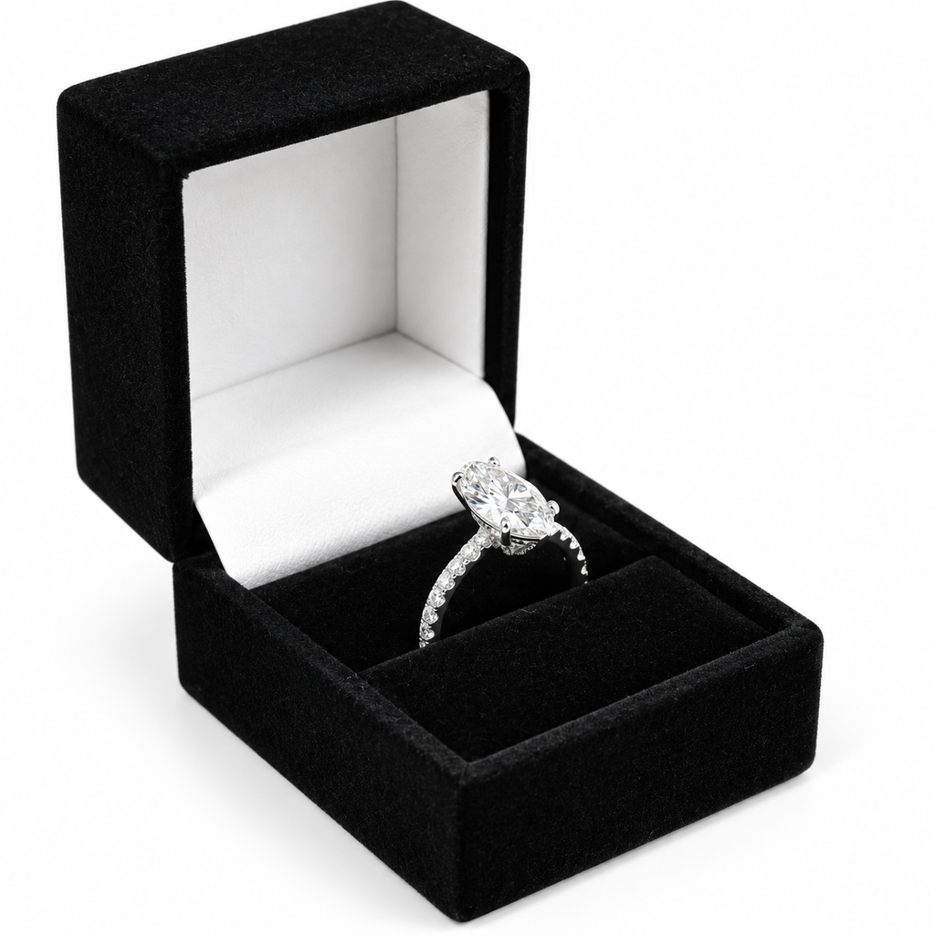 A silver-toned diamond engagement ring with a large oval center stone and pavé band, displayed inside an open black velvet ring box with a white interior on a white background.